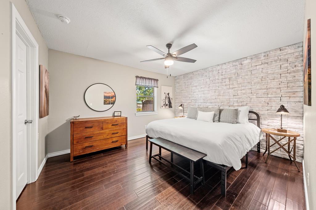 Bedroom with a large bed, pale stone accent wall, and dark wood floors.