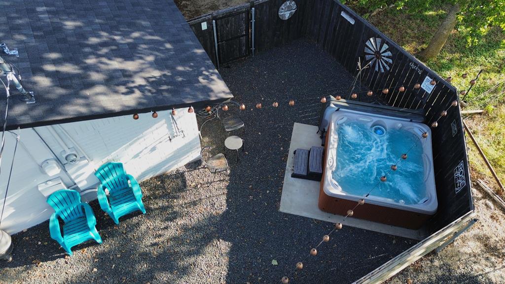 Fenced gravel patio with a bubbling hot tub, turquoise chairs, and string lights.
