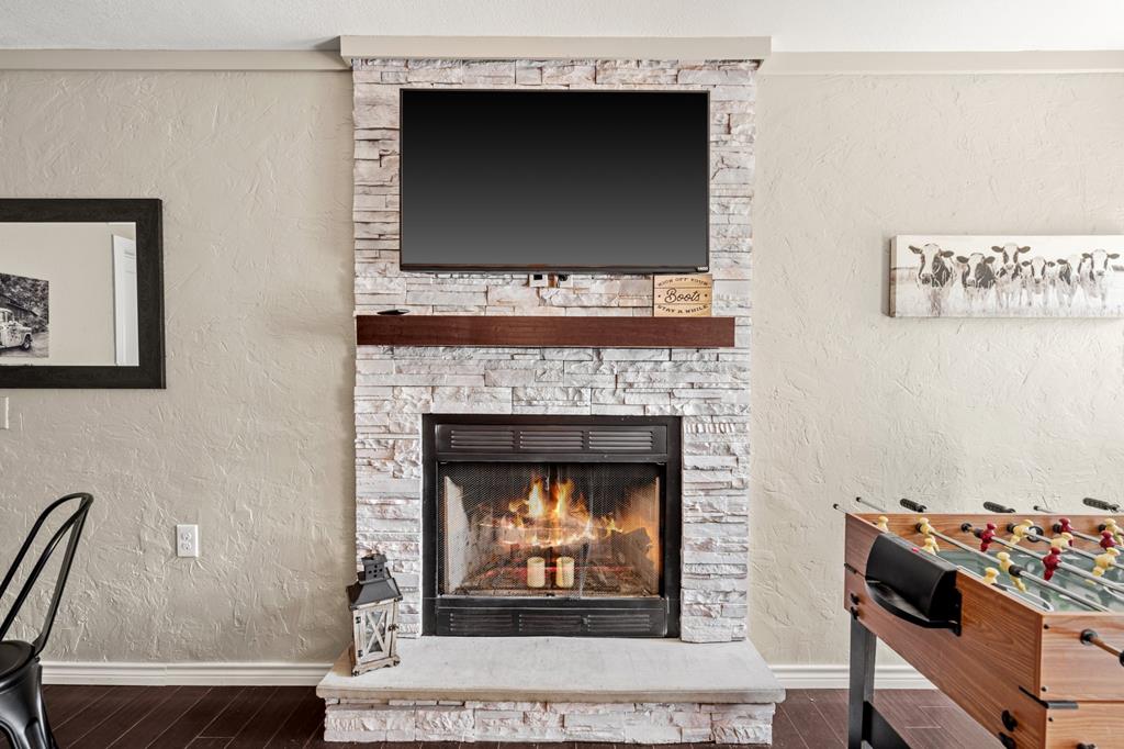 Living room with a lit stone-surround fireplace, mounted television, and foosball table.