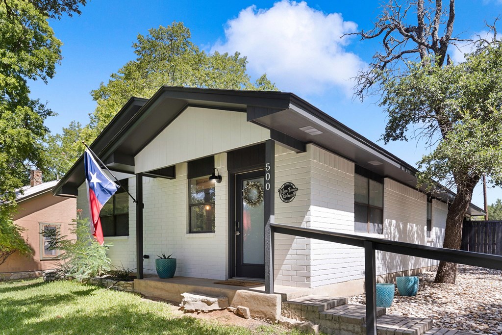 White brick house with dark trim, a Texas flag, and a covered front entrance.
