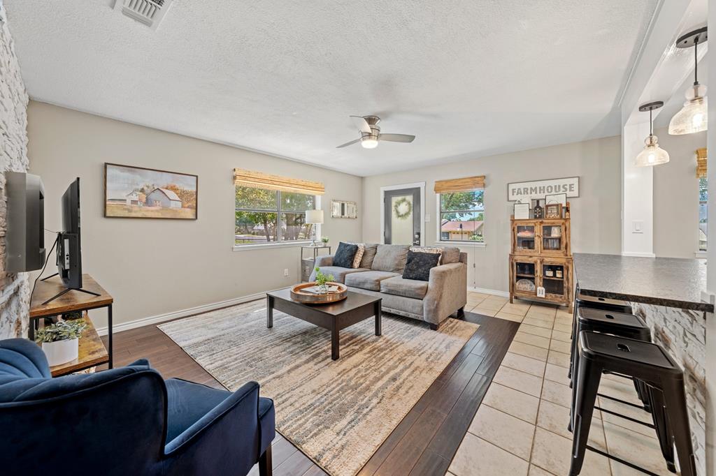 Living room with gray sectional, blue armchair, patterned rug, and kitchen counter with bar stools.