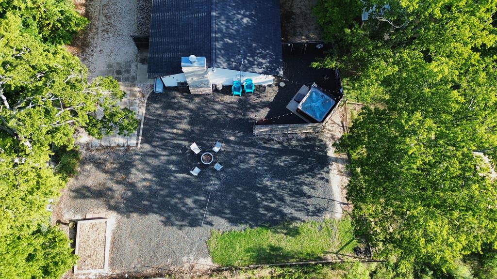 Aerial view of a gravel courtyard with a hot tub, seating, and mature trees beside the home.