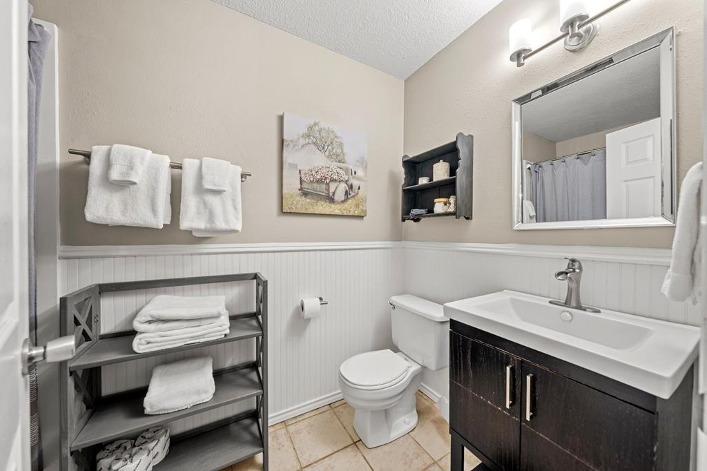Bathroom with a dark wood vanity, white sink, toilet, and beadboard wainscoting.
