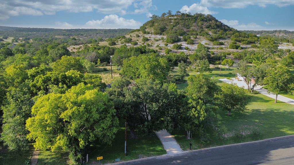 Aerial view of wooded property with a driveway, lawns, and a rocky hill beyond.