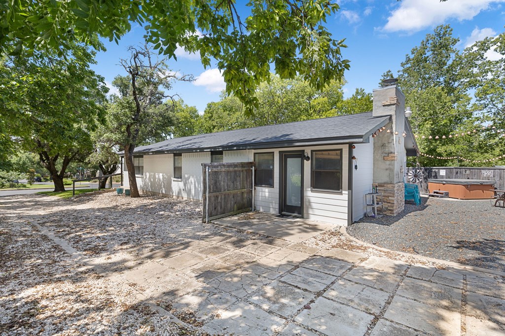 Single-story house with a stone chimney, shaded patio, and fenced hot tub area.