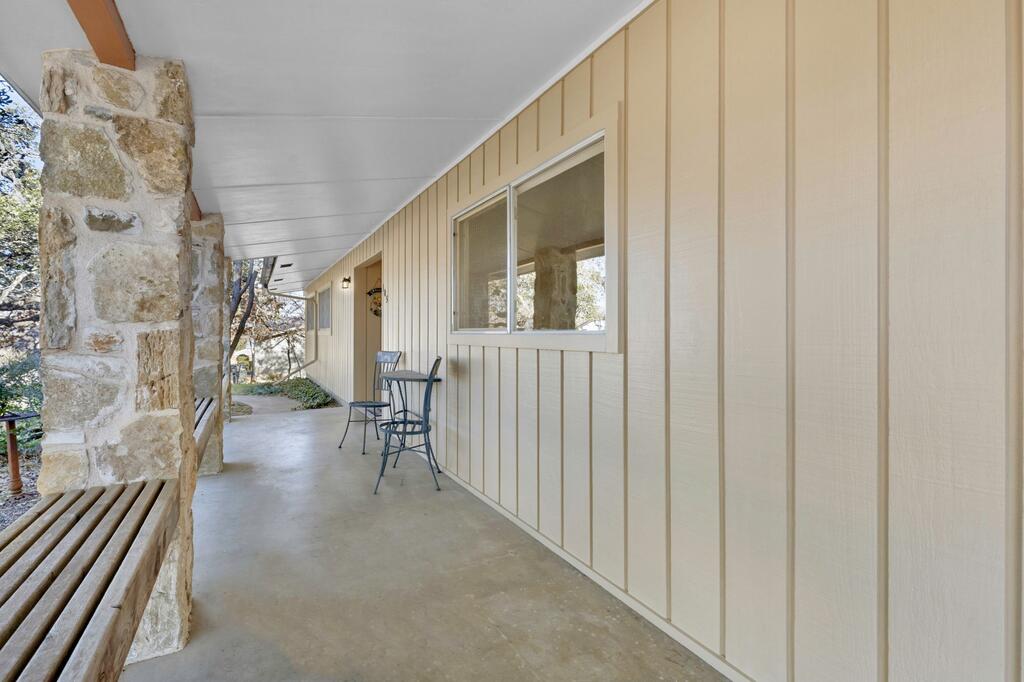 Covered porch with cream siding, a stone column, built-in bench, and metal table and chairs.