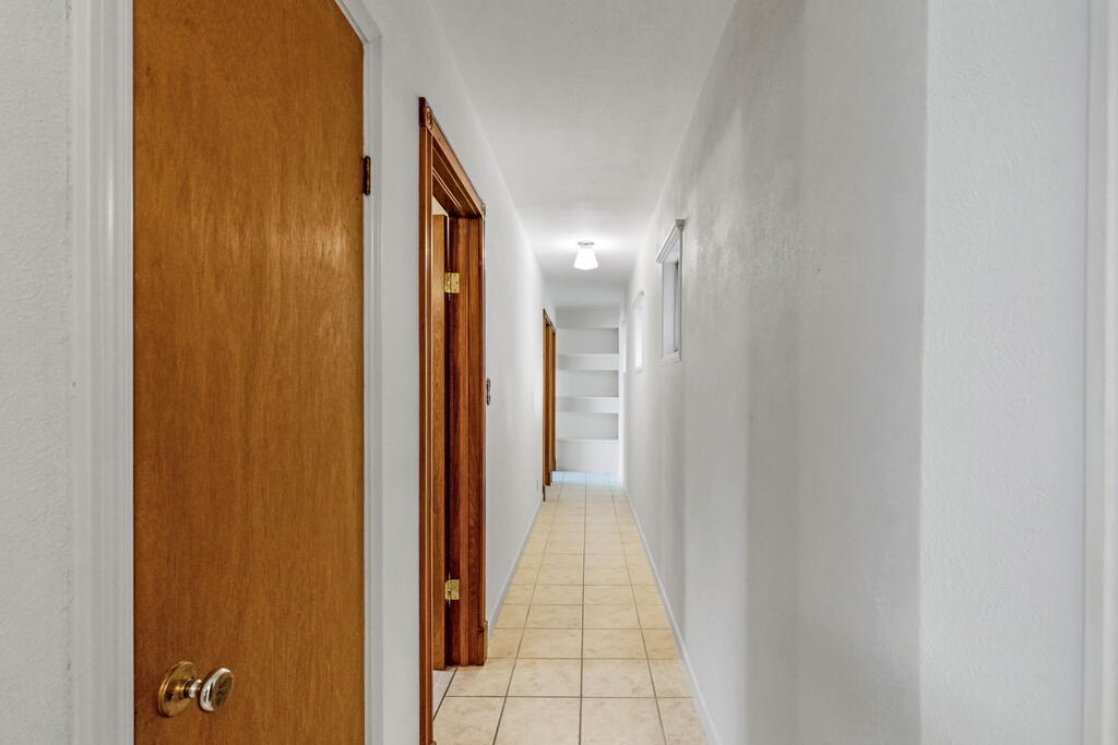 Long hallway with beige tile flooring, wooden doors, and recessed shelves at the far end.