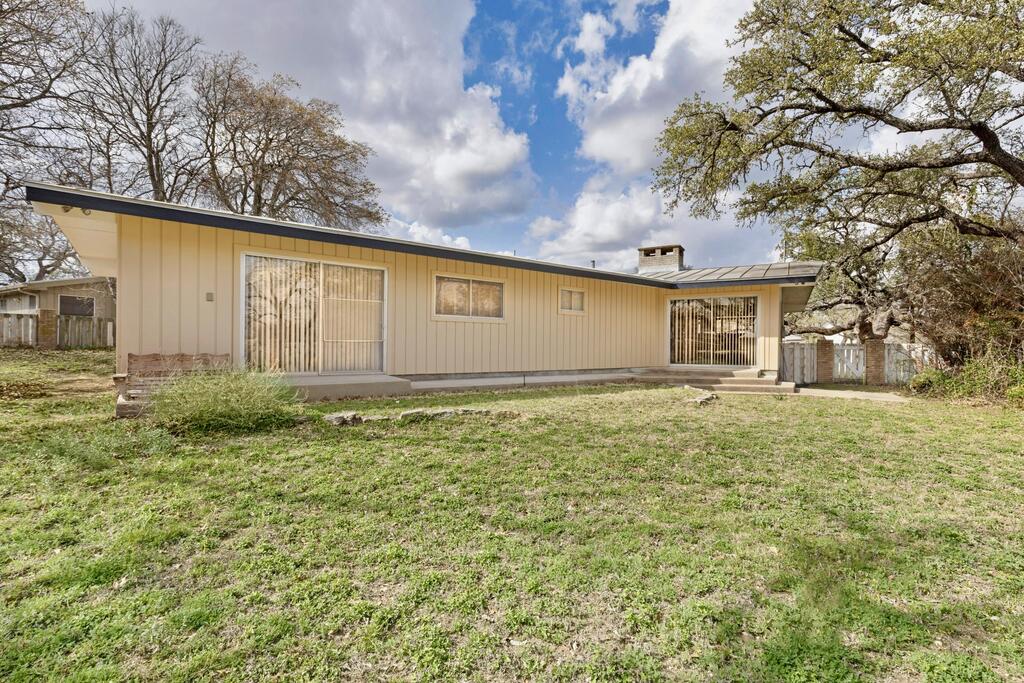 Rear of a single-story beige home with sliding glass doors and a grassy yard.