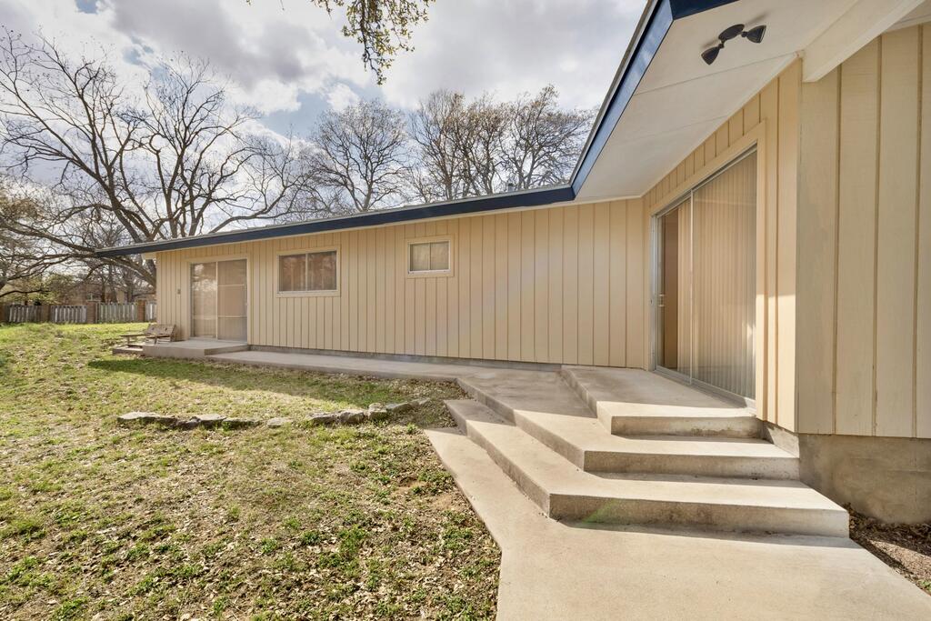 Rear exterior of a beige-sided home with broad concrete steps and a patchy yard.