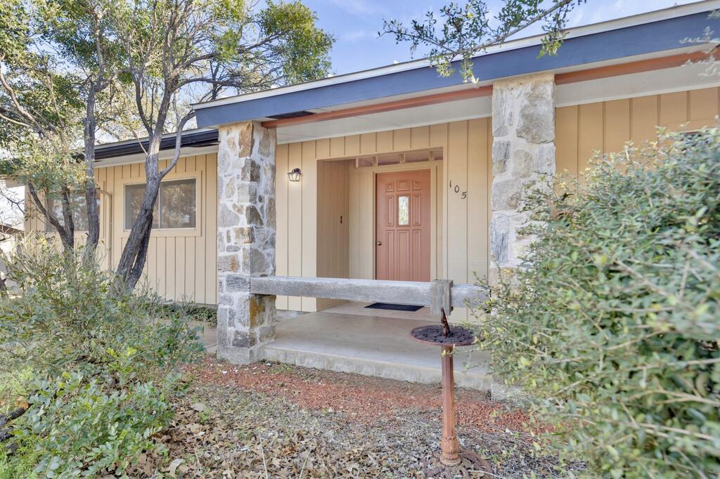 Single-story home with stone porch columns, a pink front door, and mature trees and shrubs.
