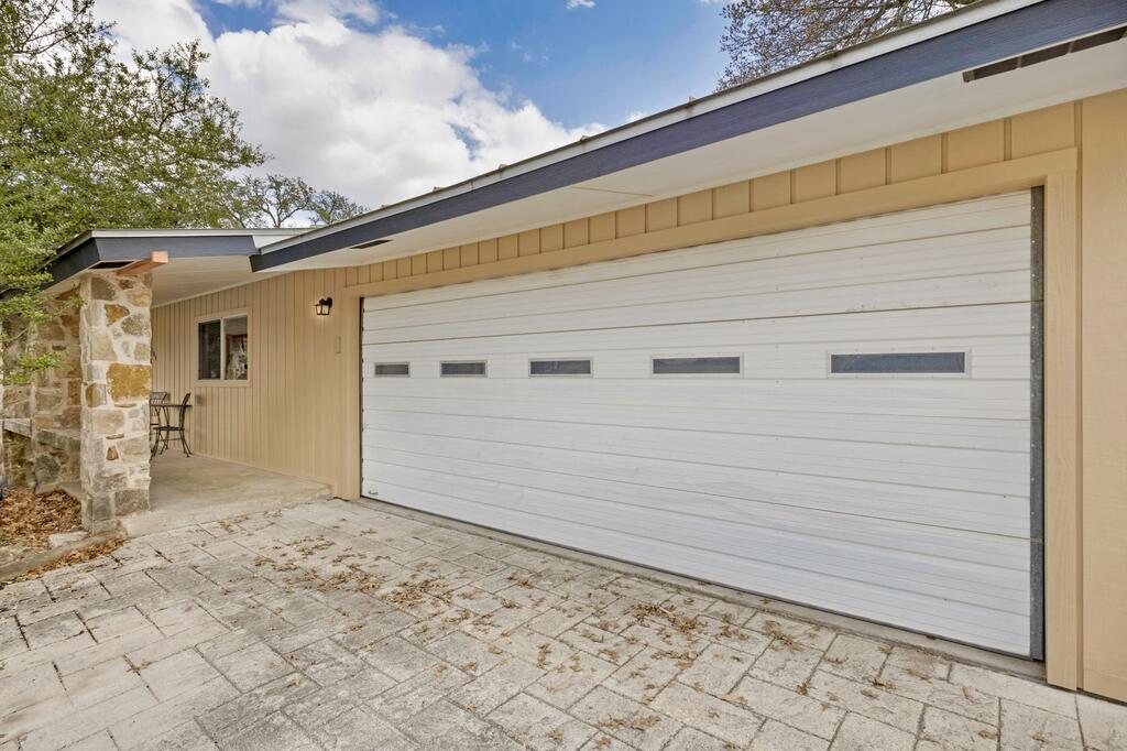 Garage exterior with a wide white door, tan siding, stone column, and paved driveway.