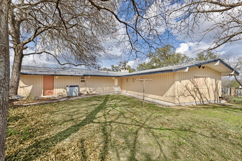 Rear of a beige single-story home beneath a large leafless tree, with an air-conditioning unit beside the house.