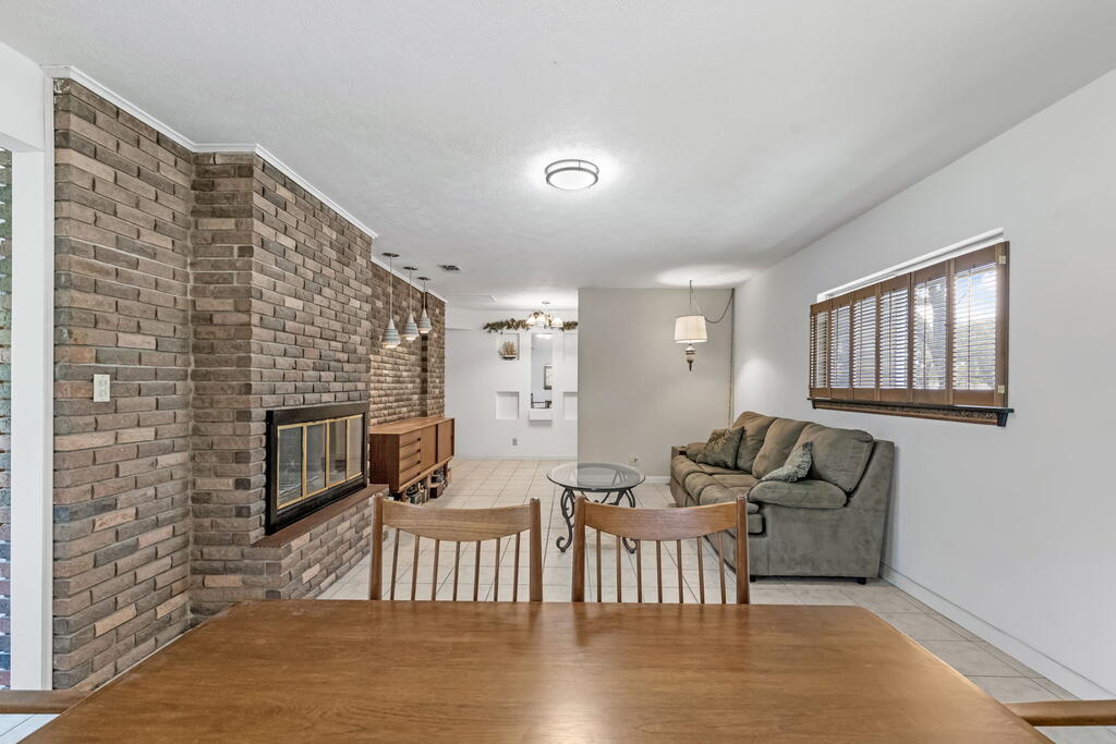 Living room with a brick fireplace, gray sofa, and wooden dining table.