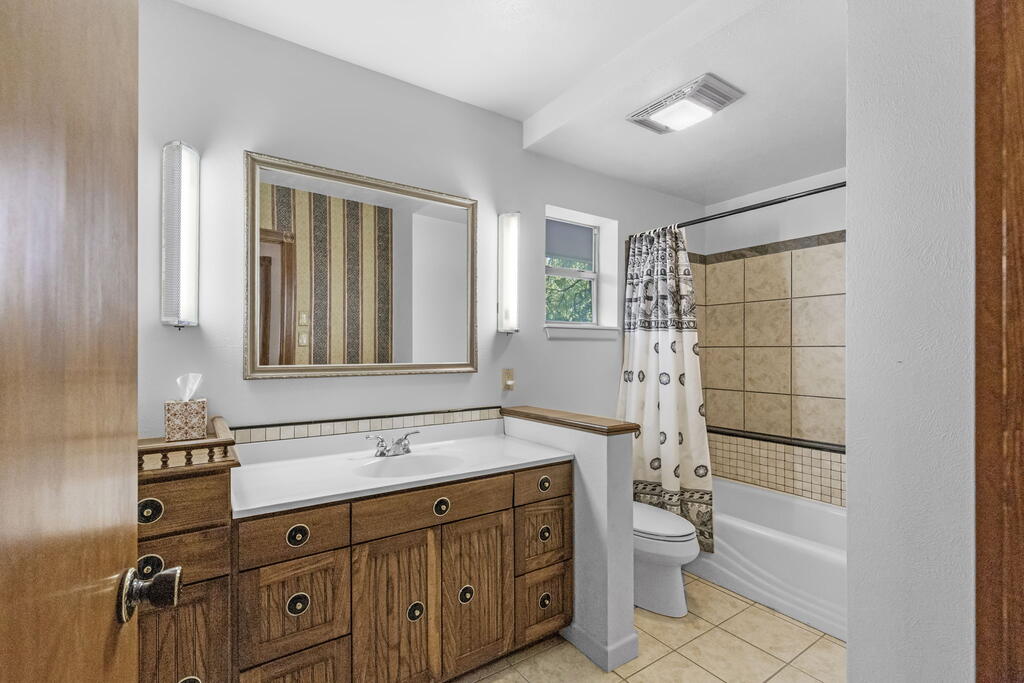 Bathroom with a wood vanity, framed mirror, and tiled tub-shower.
