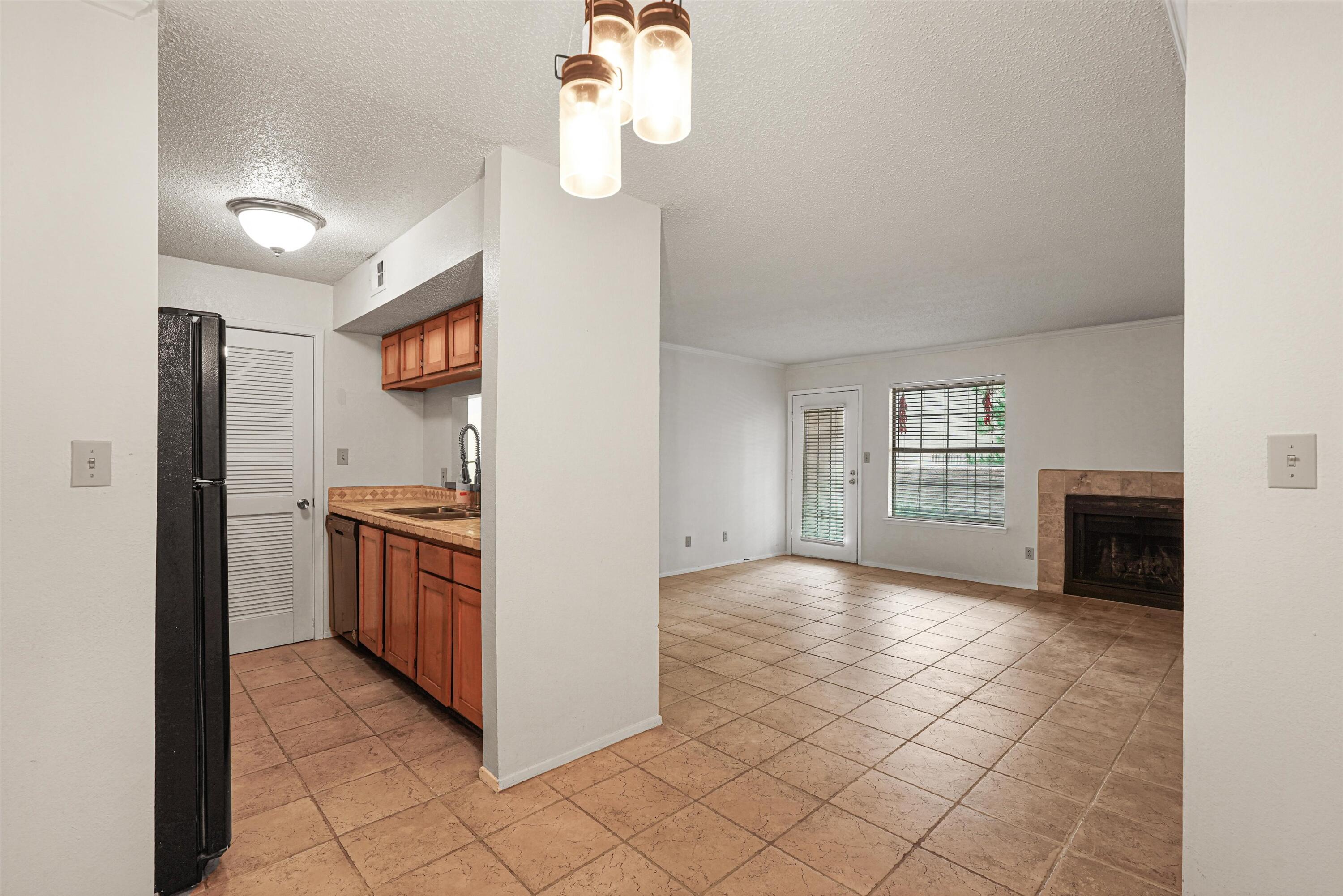 Unfurnished kitchen and living area with terracotta tile floors, wood cabinets, and a stone-surround fireplace.