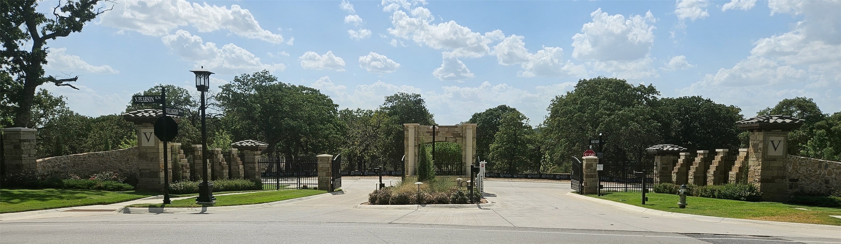 Gated community entrance with stone pillars, open iron gates, and landscaped grounds.