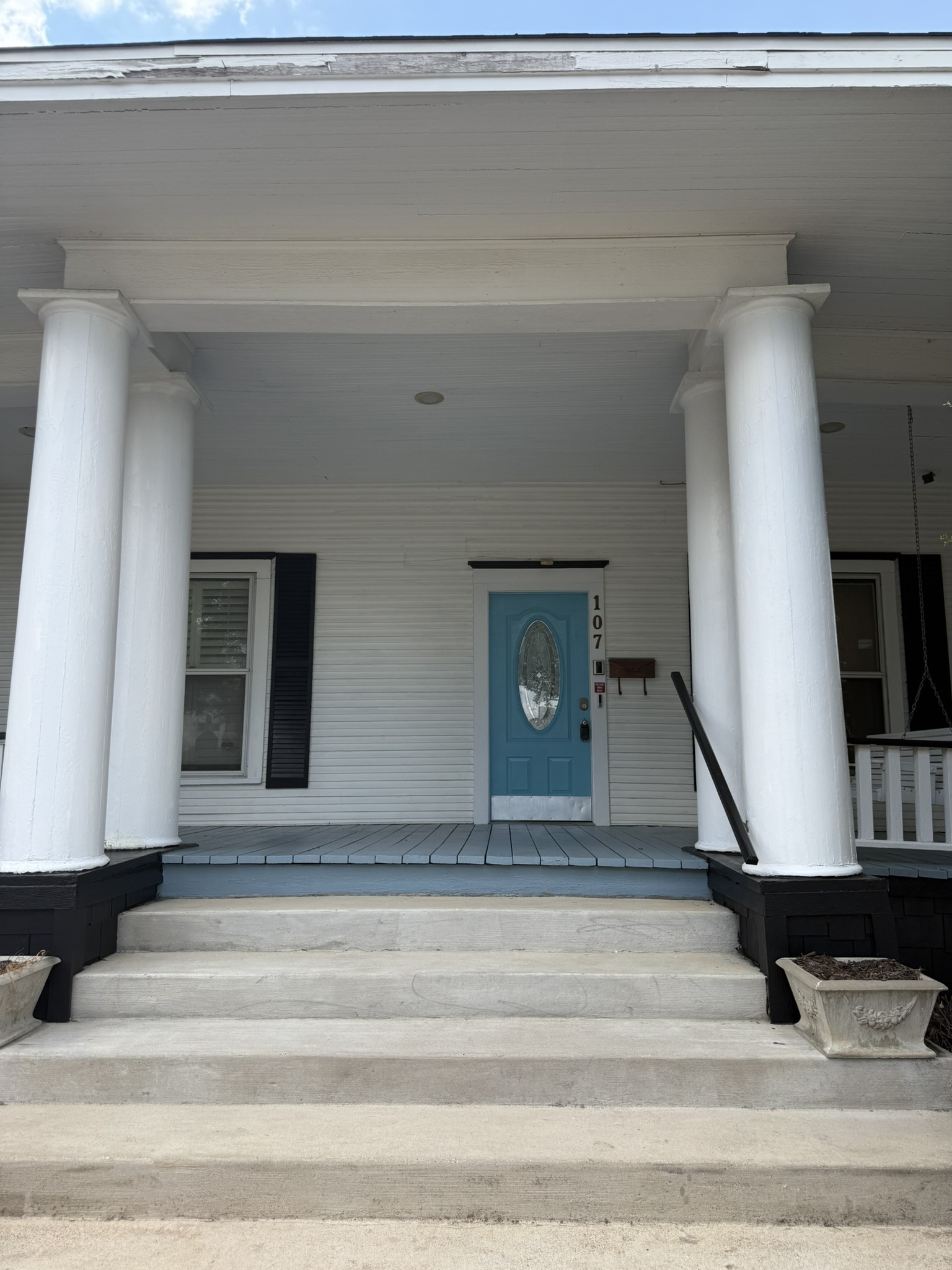 Covered front porch with white columns, concrete steps, and a blue door marked 107.