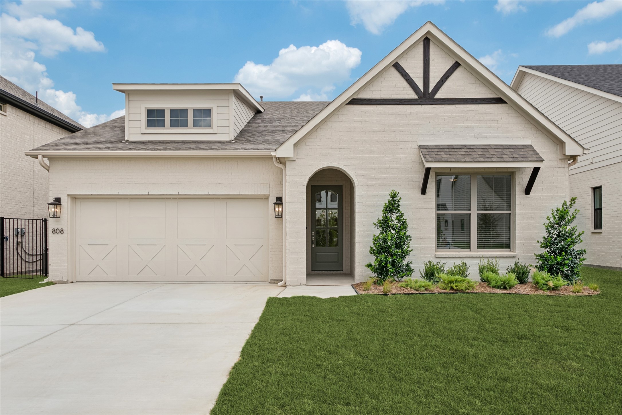 Light brick home with a two-car garage, arched entry, and dark timber accents on the front gable.