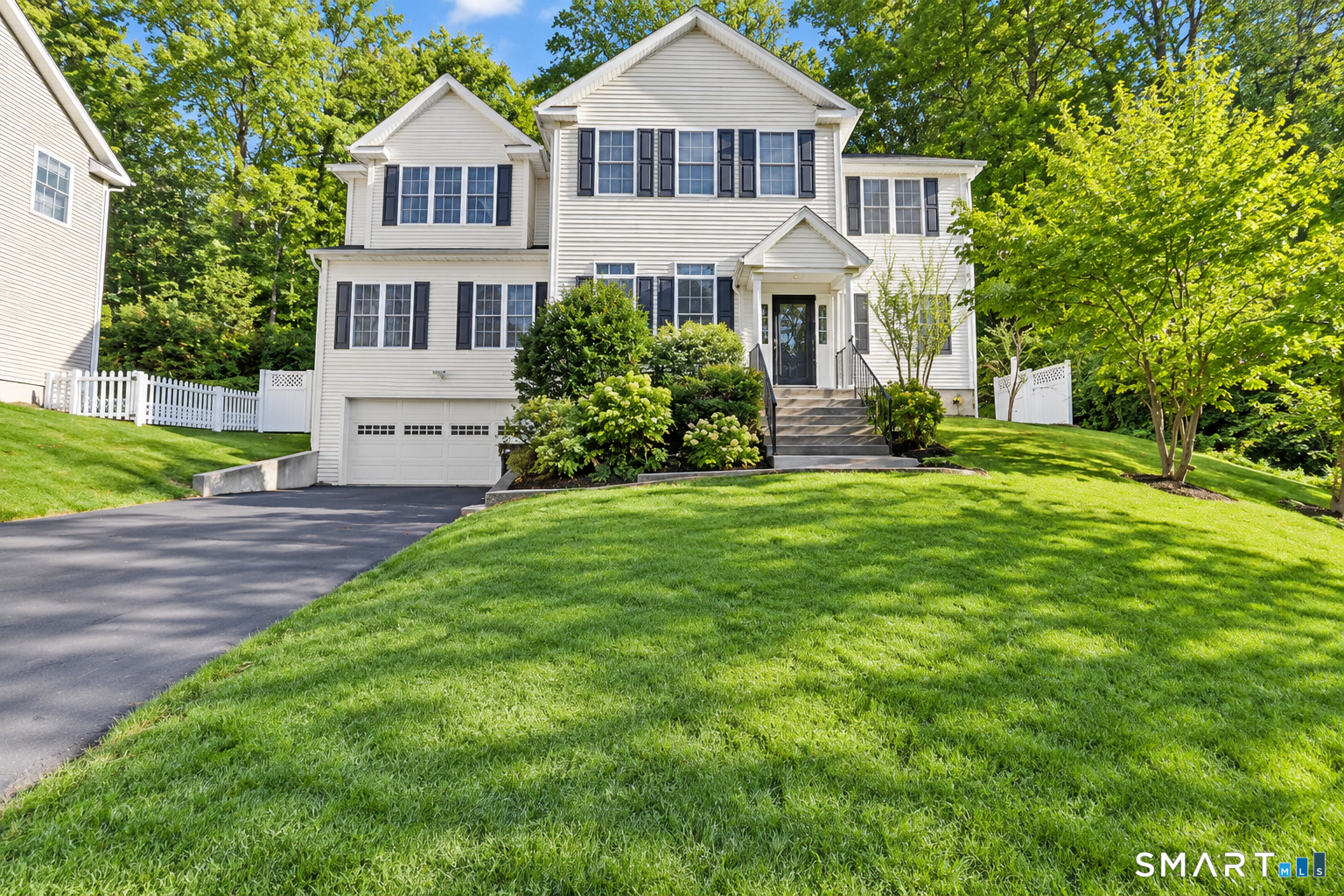 White two-story house with dark shutters, an attached garage, and a broad green lawn.