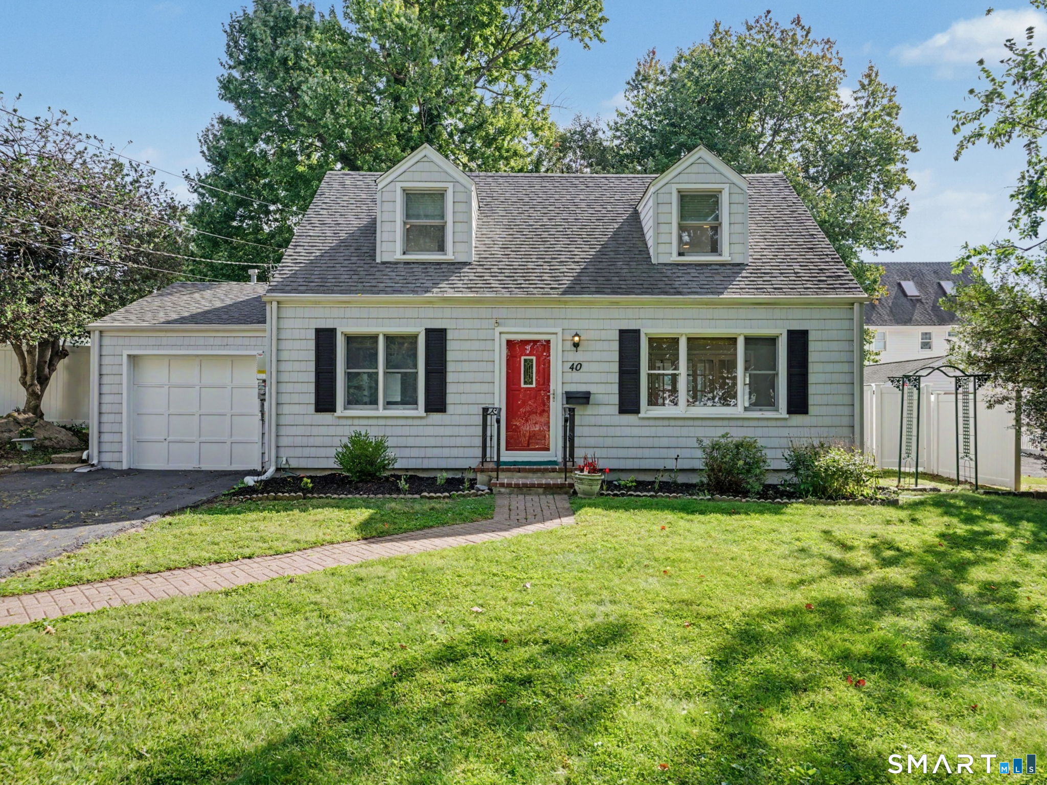 Gray shingle-sided house with a red front door, two dormers, attached garage, and broad green lawn.
