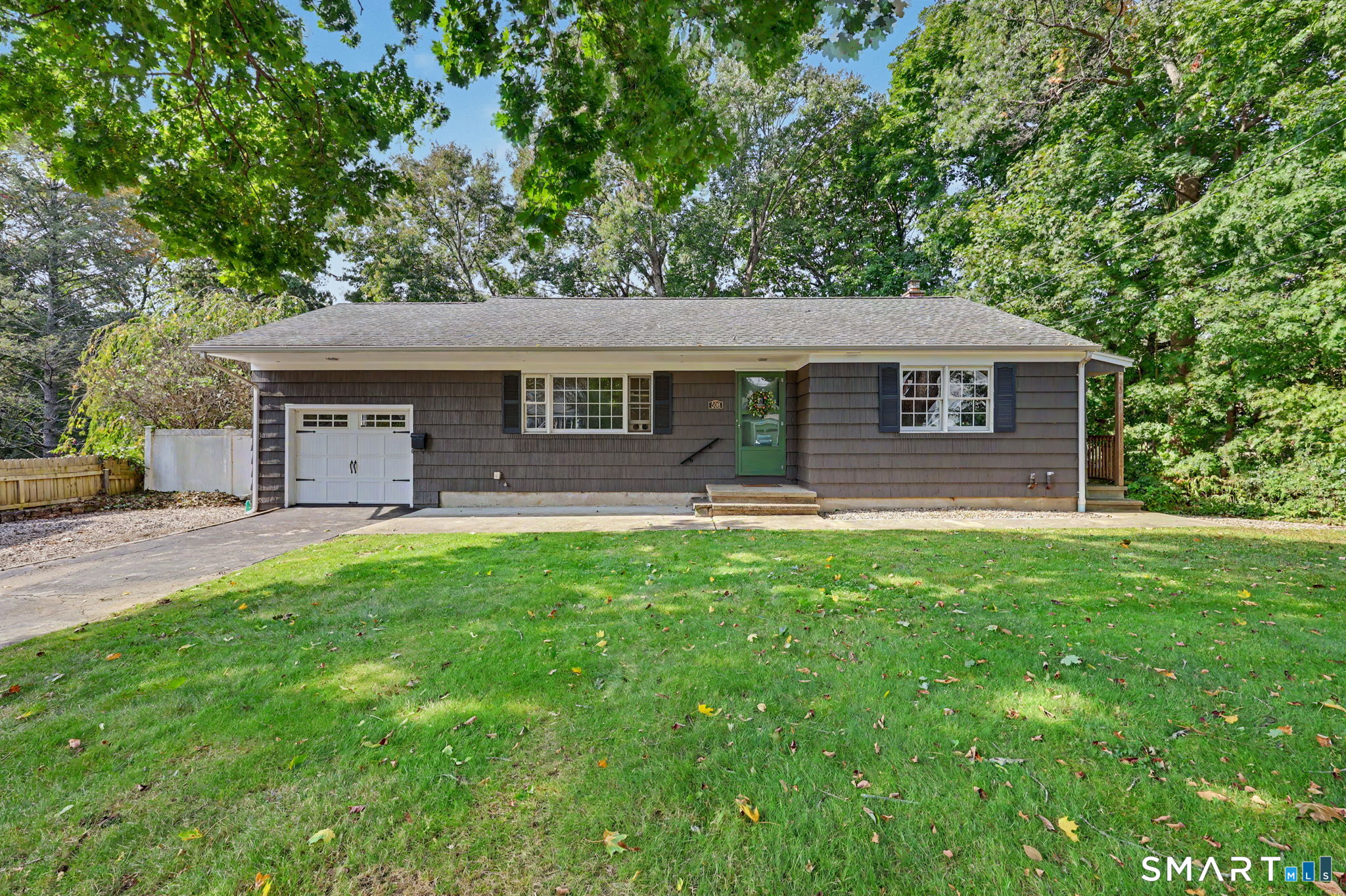 Single-story gray-shingled house with a green front door, attached garage, and spacious lawn.