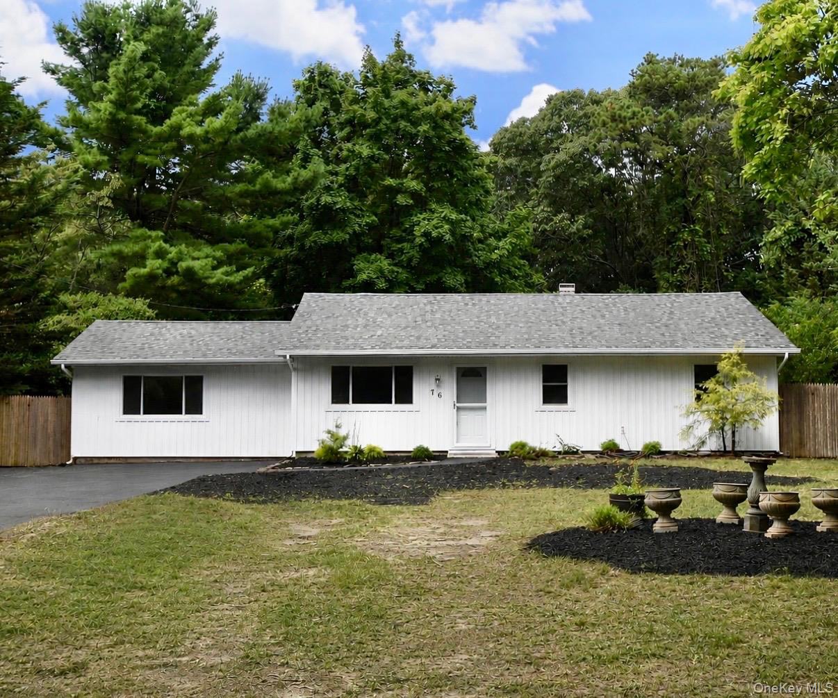 White single-story house with gray roof, broad lawn, driveway, and mature trees.