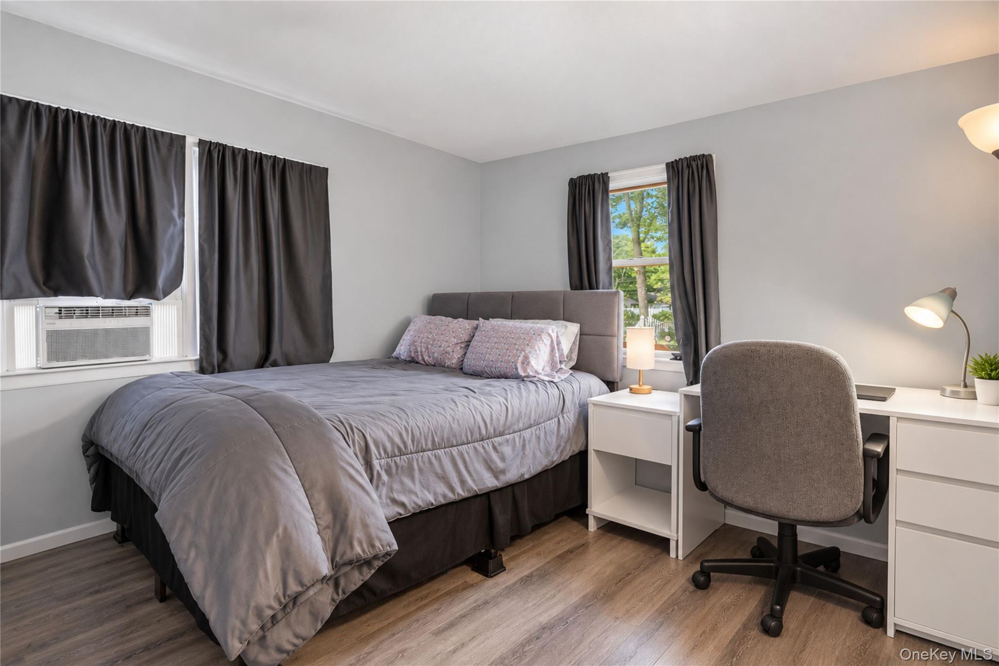Furnished bedroom with a gray bed, window air conditioner, and desk with an office chair.