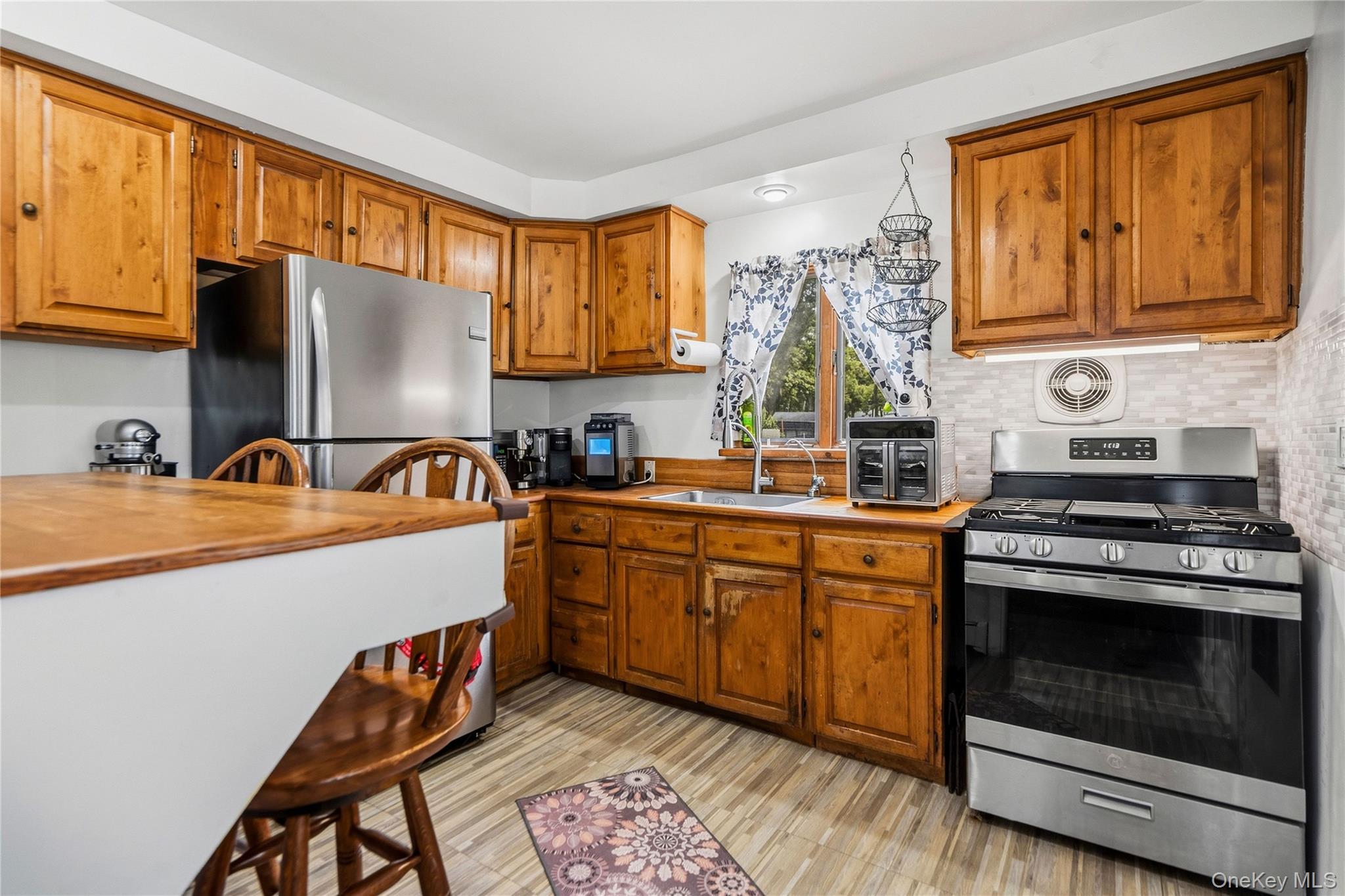 Kitchen with honey-toned wood cabinets, stainless steel appliances, and a breakfast counter.