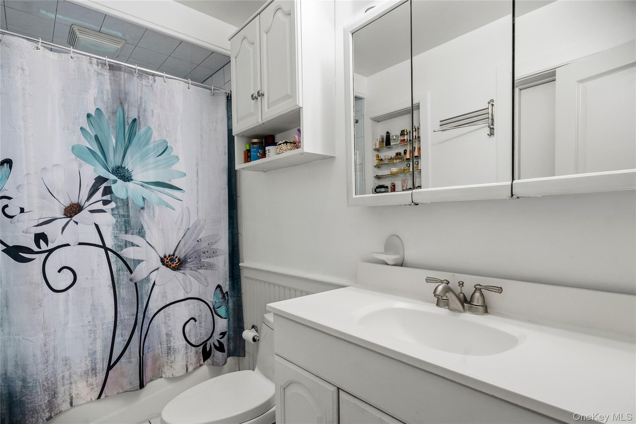 Bathroom with a white vanity and mirrored cabinets beside a large floral shower curtain.
