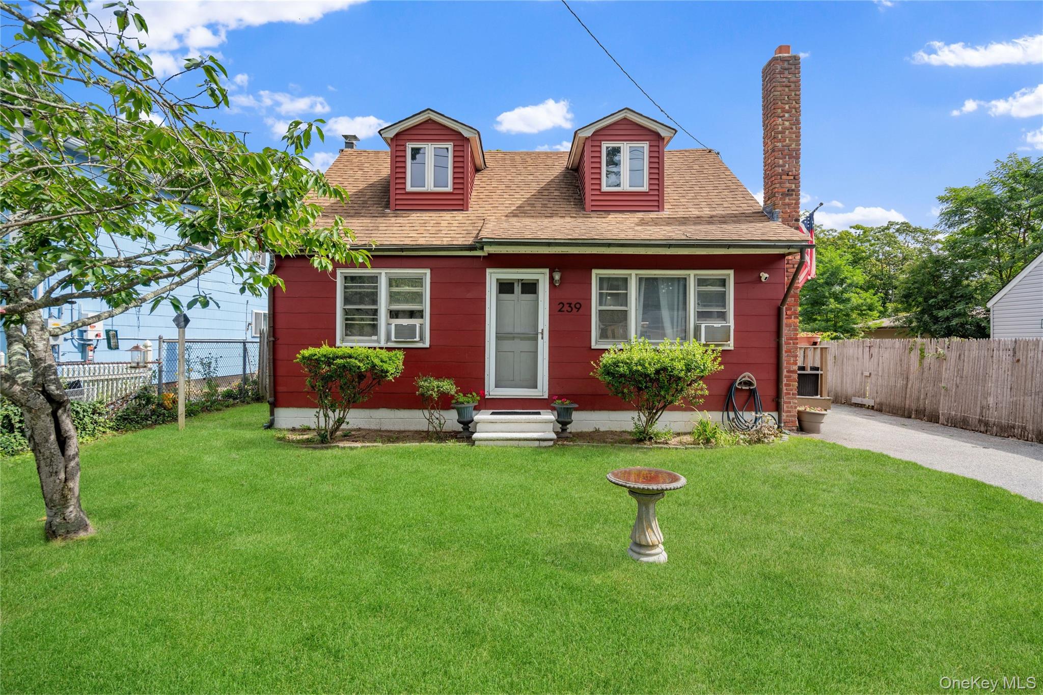 Red-sided house with twin dormers, a brick chimney, and a broad front lawn.