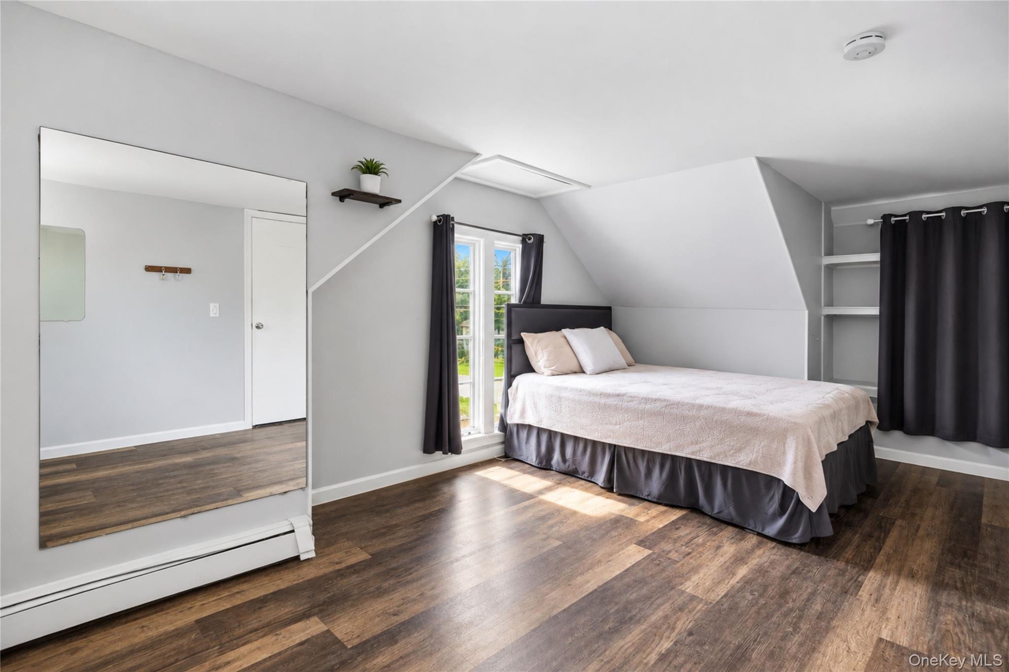 Attic bedroom with a bed beneath a sloped ceiling, narrow windows, dark curtains, and wood flooring.