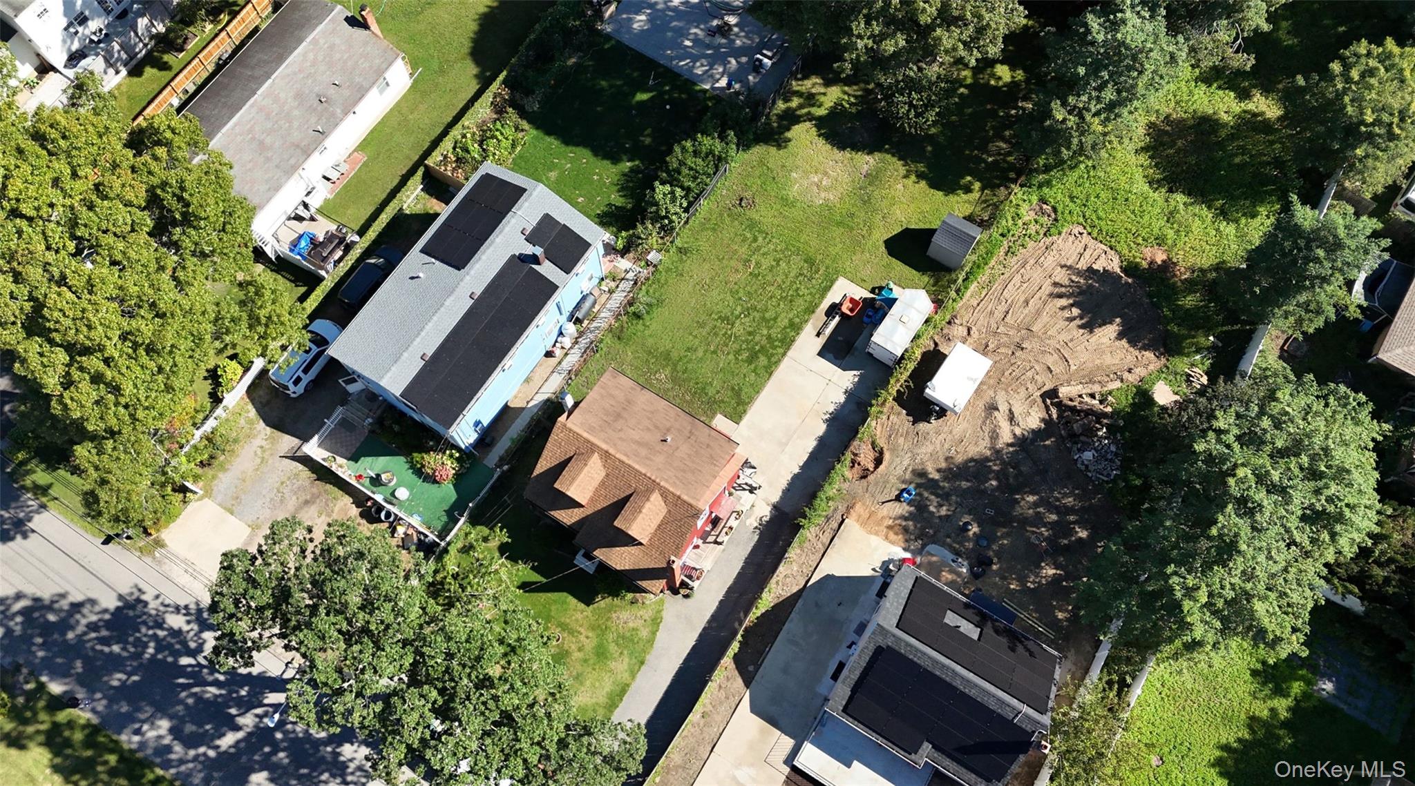 Aerial view of a blue house with rooftop solar panels beside a cleared construction lot.