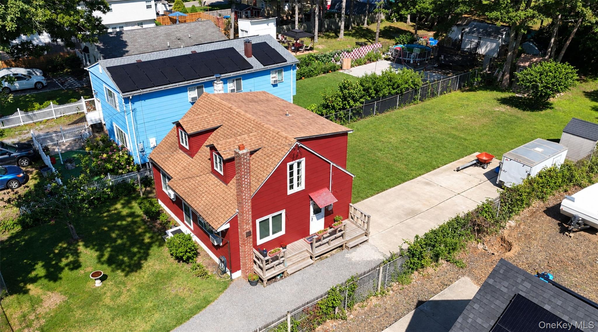 Aerial view of a red two-story house with a raised deck, broad lawn, and paved driveway.