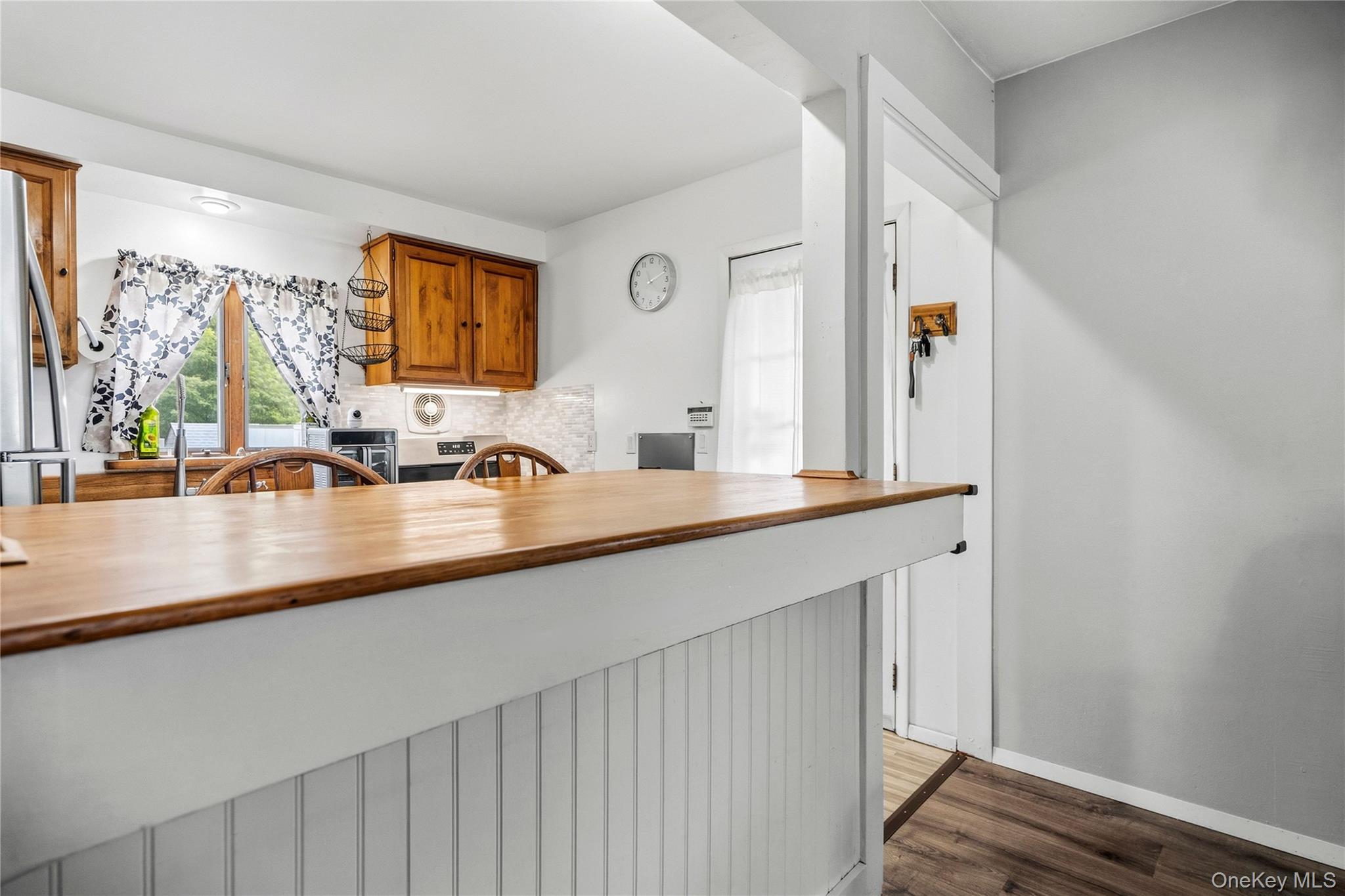 Kitchen with a long wood-topped peninsula, honey-colored cabinets, and a curtained window.
