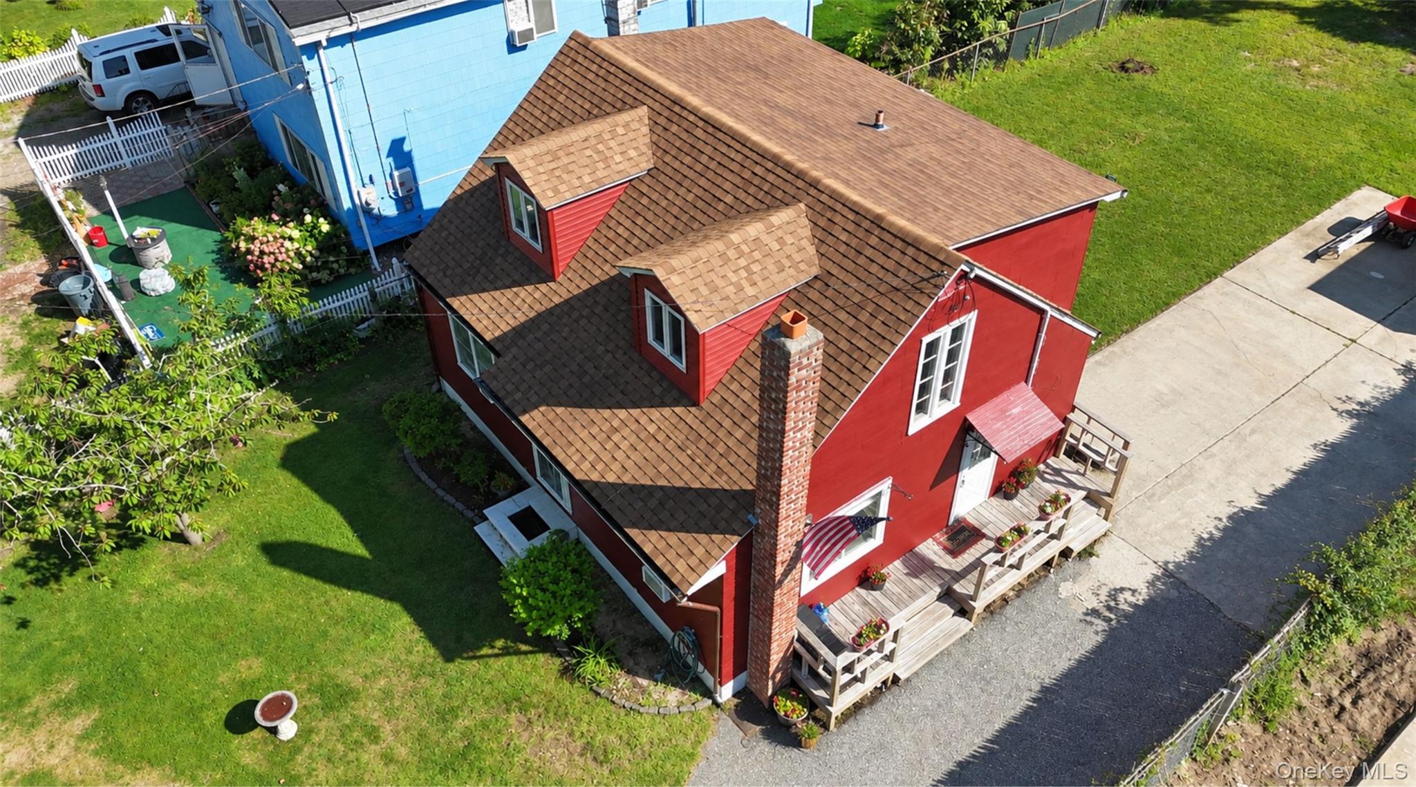 Aerial view of a red two-story house with a shingle roof and wooden deck beside a paved driveway.