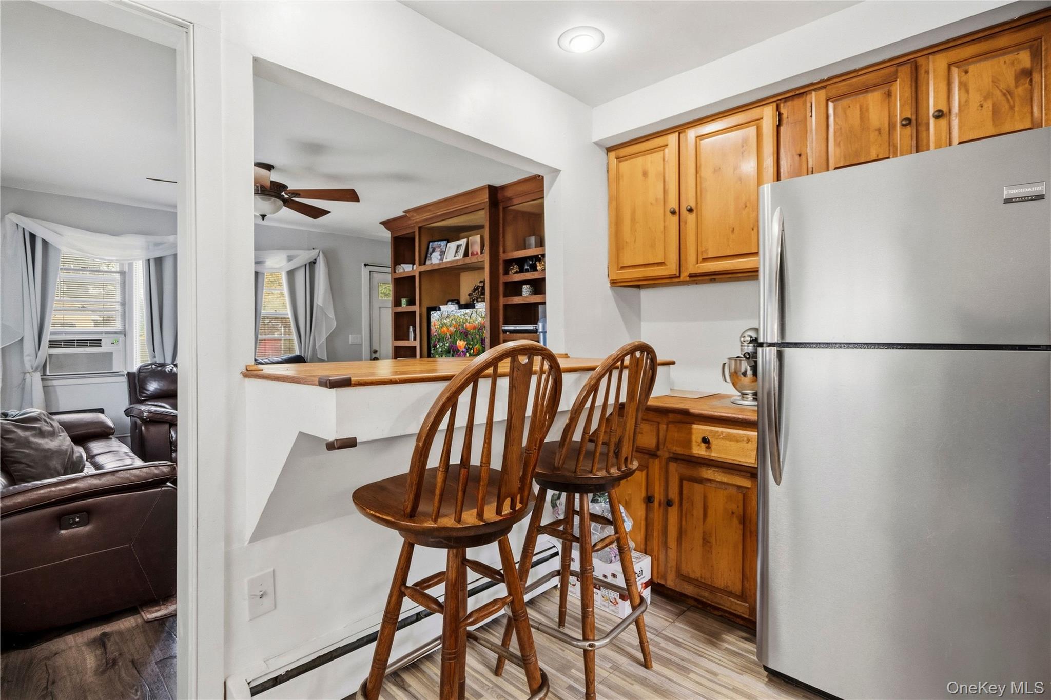 Kitchen with wooden cabinets, stainless steel refrigerator, and breakfast counter opening onto a living room.