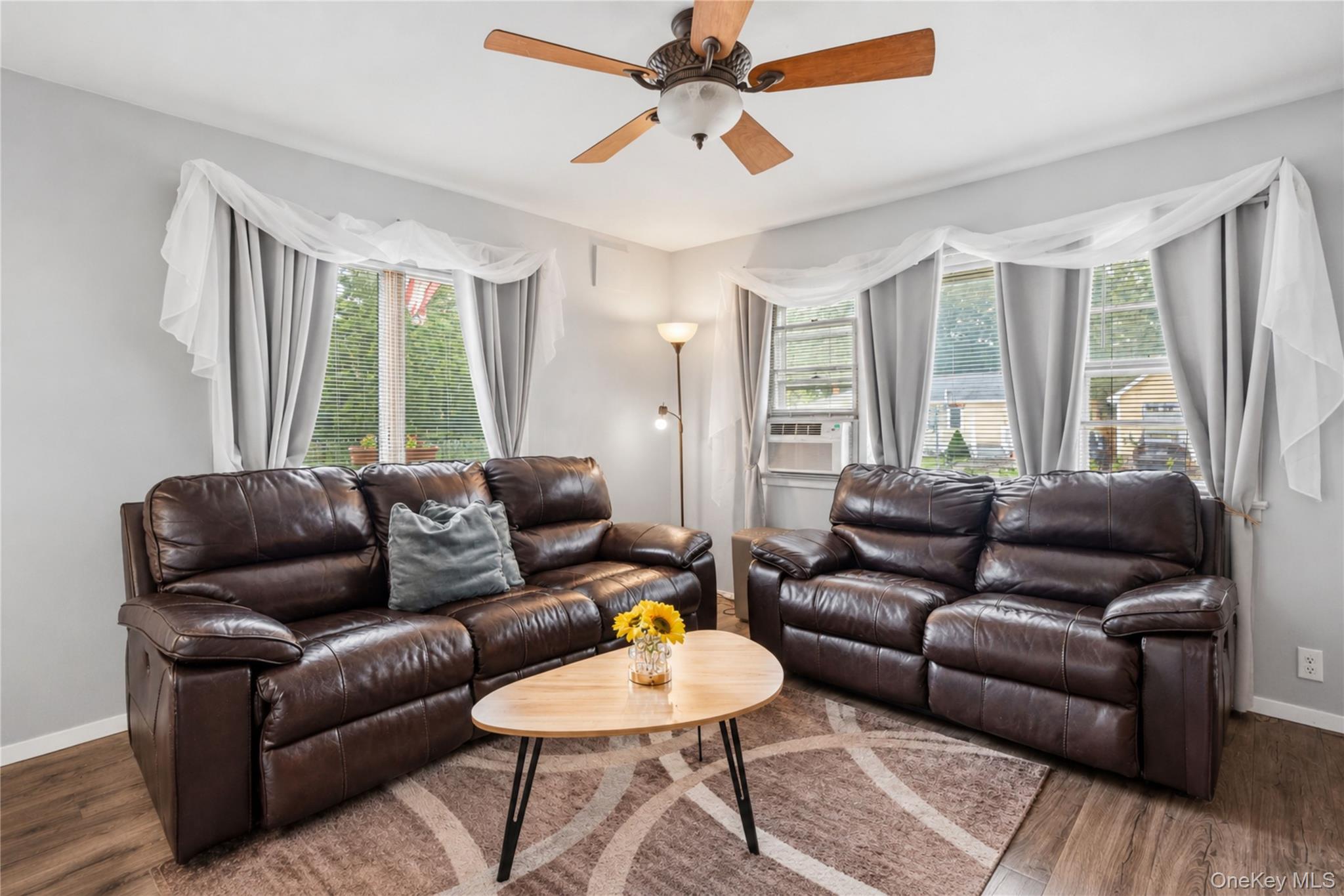 Living room with two dark leather sofas, a flower-topped coffee table, and curtained windows.