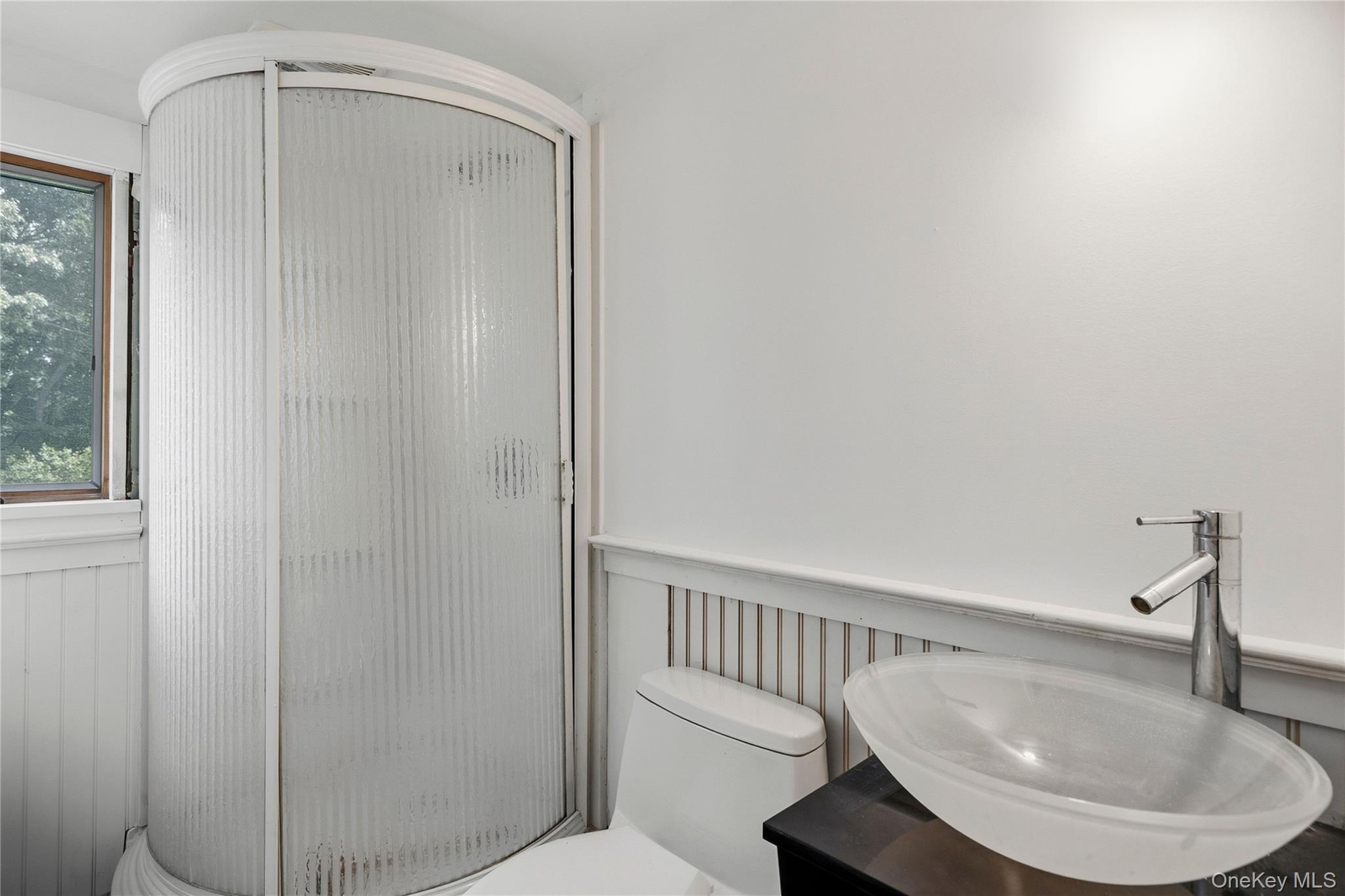 Bathroom with a curved frosted-glass shower, vessel sink, and window overlooking trees.