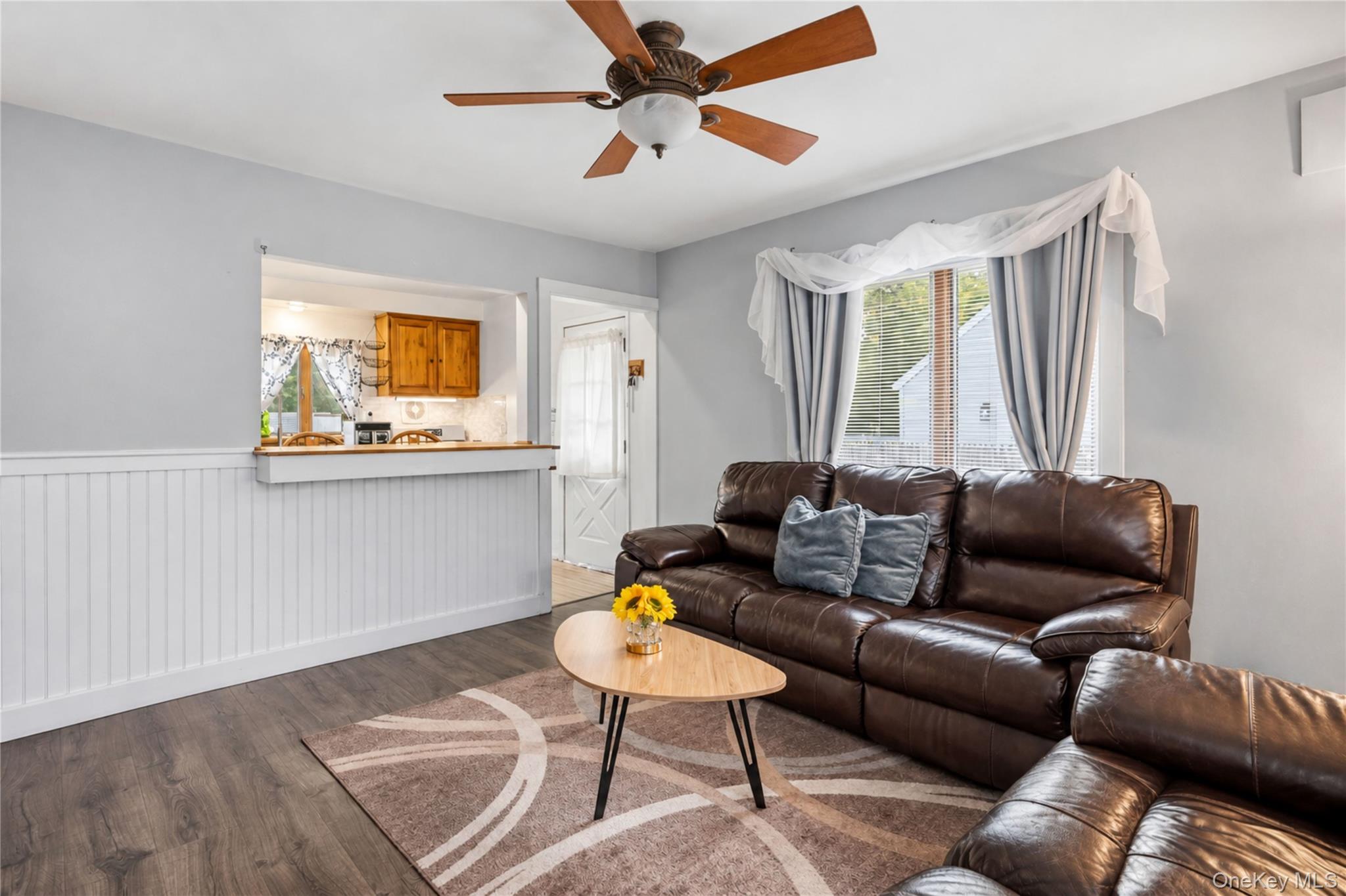 Living room with a brown leather sectional, patterned rug, and open view into the kitchen.