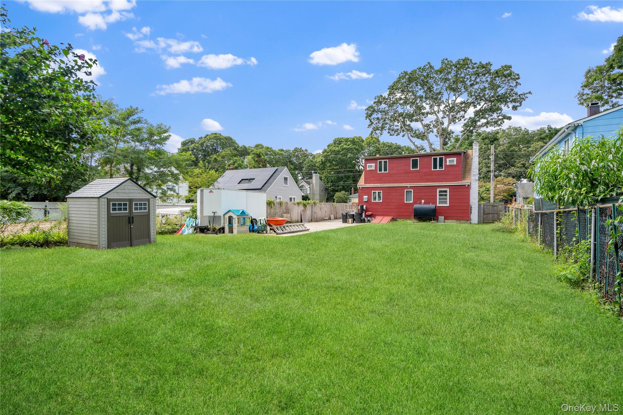 Backyard with a broad lawn, gray storage shed, and children’s play equipment.