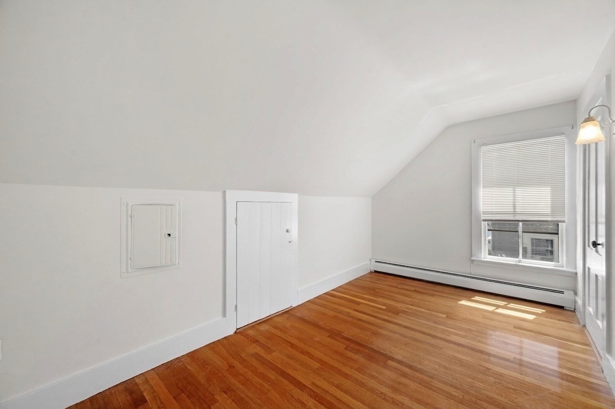 Empty room with a sloped ceiling, polished hardwood floors, and a window with blinds.