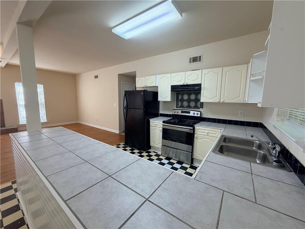 Kitchen with broad tiled peninsula, white cabinets, stainless range, and checkerboard floor.