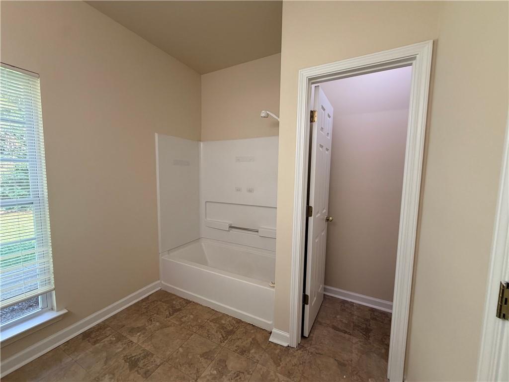 Bathroom with a white bathtub, patterned tile floor, and window with blinds.