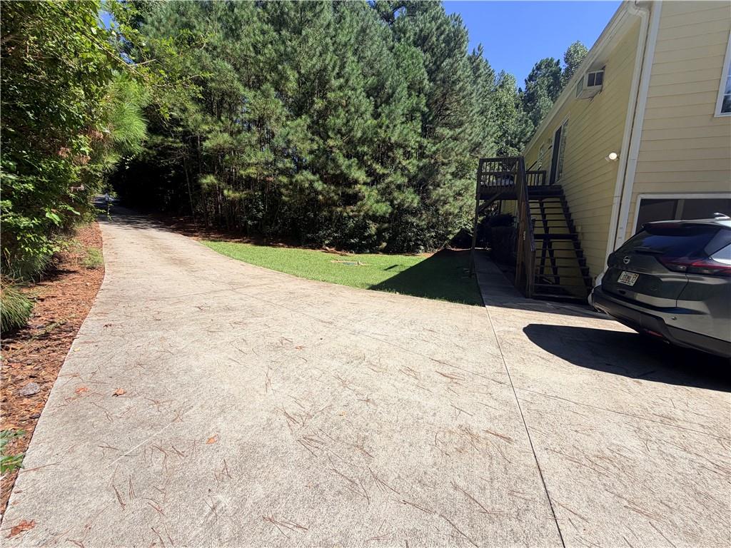 Concrete driveway beside a light-colored house, with an exterior staircase and dense pine trees.