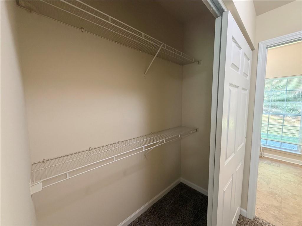 Empty walk-in closet with two levels of white wire shelving and dark carpet.
