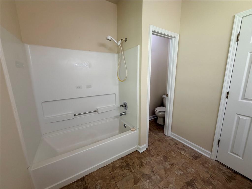 Bathroom with a white tub and shower, grab bar, brown tile floor, and separate toilet room.