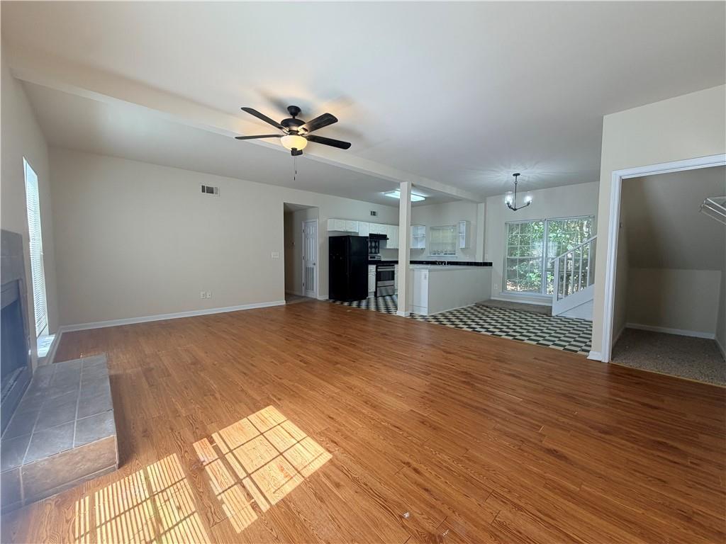 Open living room with wood floors, tiled fireplace, ceiling fan, and adjoining checkerboard-floor kitchen.