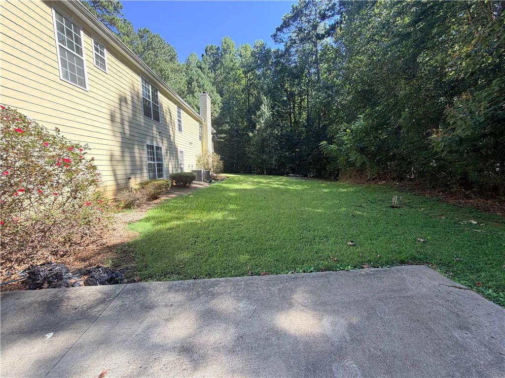 Side yard with a broad lawn beside a yellow-sided house and mature trees.