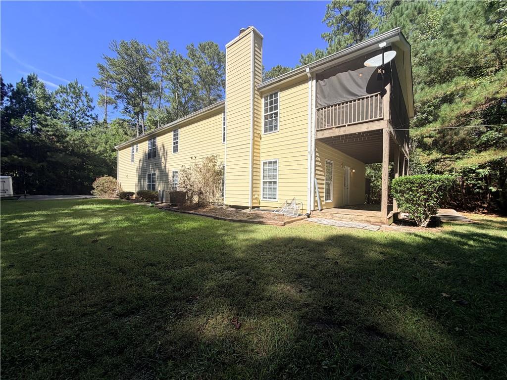 Yellow two-story house with a raised covered deck and balcony overlooking a broad lawn.