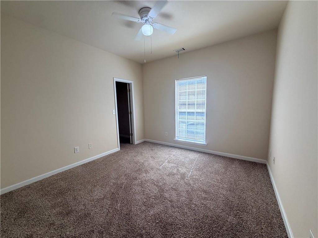 Empty carpeted bedroom with a ceiling fan and a window with blinds.
